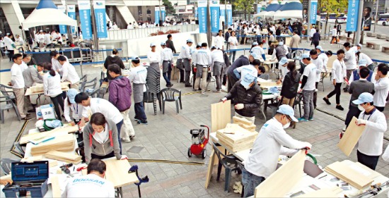 박용만 회장을 비롯한 두산 임직원 200여명이 지난 10월24일 ‘두산인 봉사의 날’ 행사를 맞아 서울 중구 장충단로 두산타워 광장에서 저소득층 가정에 전달할 가구를 만들고 있다.  두산 제공 