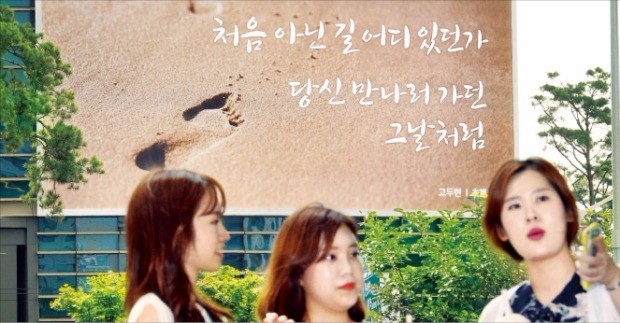 에쓰오일이 서울 공덕동 본사 외벽에 설치한 대형 글판에 고두현 시인의 시 ‘초행’이 실렸다. 주변 직장인들이 23일 글판 앞에서 이야기를 나누고 있다. 김영우 기자 youngwoo@hankyung.com 