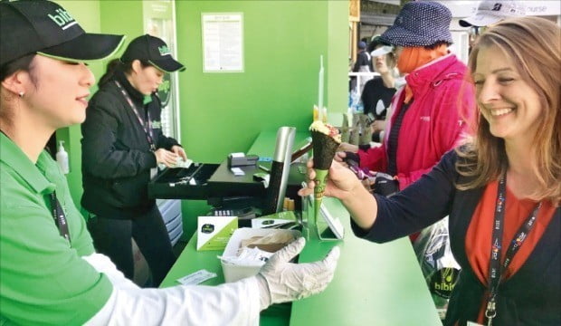 < 아이스크림 모양 비빔밥 인기 > 21일 끝난 미국프로골프(PGA) 투어인 ‘더 CJ컵 @ 나인브릿지’에 마련된 비비고 부스에서 한 외국인이 아이스크림콘 모양의 비빔밥인 ‘비비콘’을 받아들고 있다. 대회 메인 스폰서로 참여한 CJ제일제당은 네 개의 코스와 갤러리플라자 엑스포존 등에서 한식을 알렸다. 나흘 동안 총 5000개의 메뉴가 판매됐다고 회사 측은 밝혔다.  /CJ제일제당 제공 