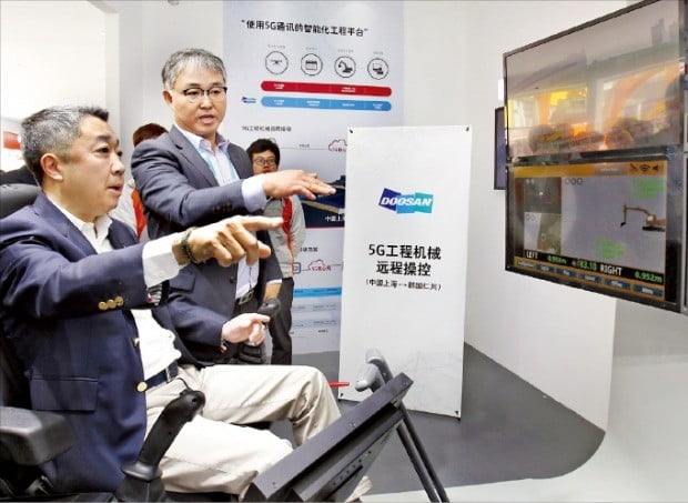 박정원 두산그룹 회장(왼쪽)이 중국 상하이에서 열린 건설기계 전시회인 ‘바우마 차이나 2018’을 찾아 5G 원격제어 기술을 이용해 인천에 있는 굴착기를 원격으로 작동시키고 있다.   /두산그룹 제공 