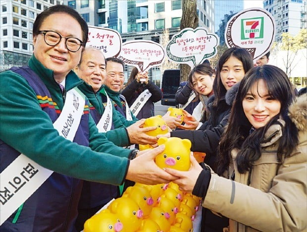 정승인 세븐일레븐 대표(왼쪽)와 점포 경영주들이 2일 서울 세종대로카페점 앞에서 고객들에게 새해 인사와 함께 황금돼지 저금통을 나눠주고 있다.
 
