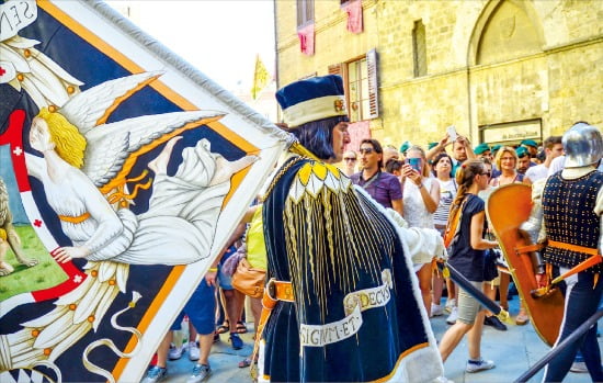 콘트라다(자치구)를 상징하는 깃발과 중세 복장을 하고 거리를 행진하는 남성 