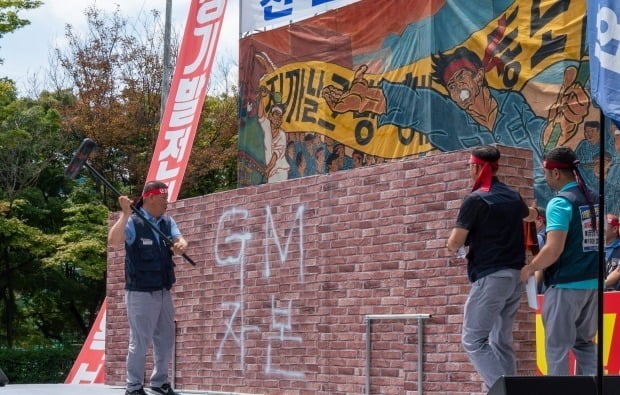 한국GM노조가 총력투쟁 결의대회를 열고 'GM자본'이라 적힌 벽을 부수는 퍼포먼스를 하고 있다.