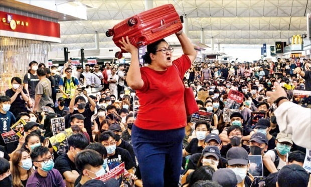 < 또 공항 점거…‘폭풍전야’ 홍콩 > ‘범죄인 인도법 개정안’(일명 송환법)에 반대하는 홍콩 시민들이 전날에 이어 13일에도 홍콩국제공항에 모여 시위를 벌였다. 시위대가 공항을 점거해 홍콩국제공항 측은 이날 오후 4시30분 이후 출발하는 모든 항공편의 운항을 중단했다. 홍콩국제공항에선 전날 230여 편에 이어 이날도 300편 이상의 비행기가 결항했다. 한 여행객(가운데)이 시위대를 뚫고 출국장에 들어가려 애쓰고 있다. /AFP연합뉴스