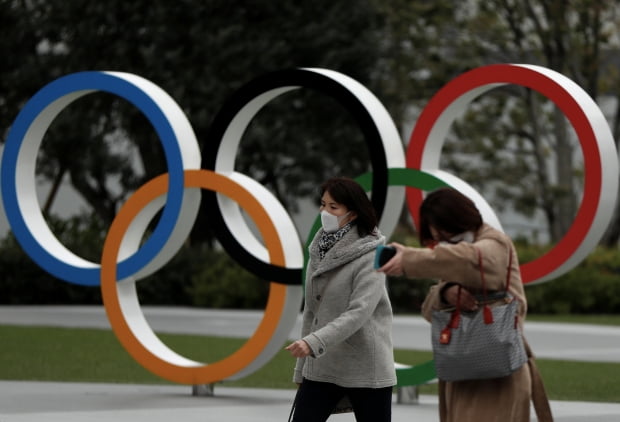 (도쿄 로이터=연합뉴스) 일본 도쿄의 올림픽박물관 앞에 설치된 오륜 조형물 앞을 30일 마스크를 쓴 행인들이 지나가고 있다. 일본 언론에 따르면 도쿄도와 대회조직위원회, 일본 정부는 이날 국제올림픽위원회(IOC)와 신종 코로나바이러스 감염증(코로나19)으로 연기된 2020도쿄올림픽을 내년 7월 23일 개막하는 것으로 합의했다. 2020-03-30