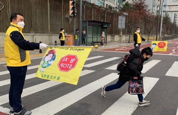 일시정지 안전깃발을 든 쌍용차 임직원들이 초등학생들의 보행 안전을 지도하고 있다. 사진=쌍용차