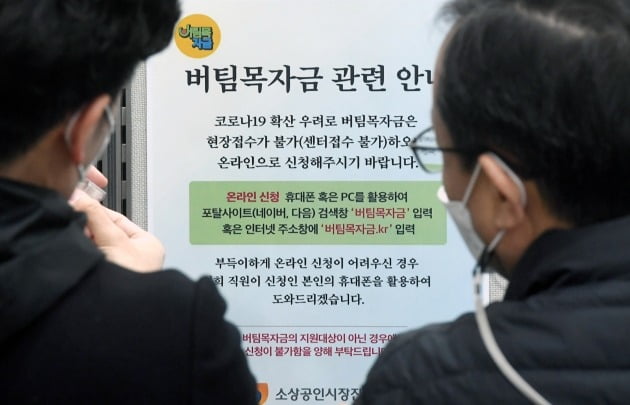 '버팀목자금'(3차 재난지원금) 신청 접수가 시작된 지난 11일 소상공인시장진흥공단 서울중부센터에서 관계자들이 안내문을 부착하고 있다. 허문찬기자  sweat@hankyung.com