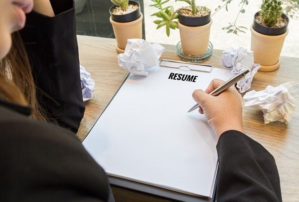 Woman hand writting resume in notebook with pen and paper balls.