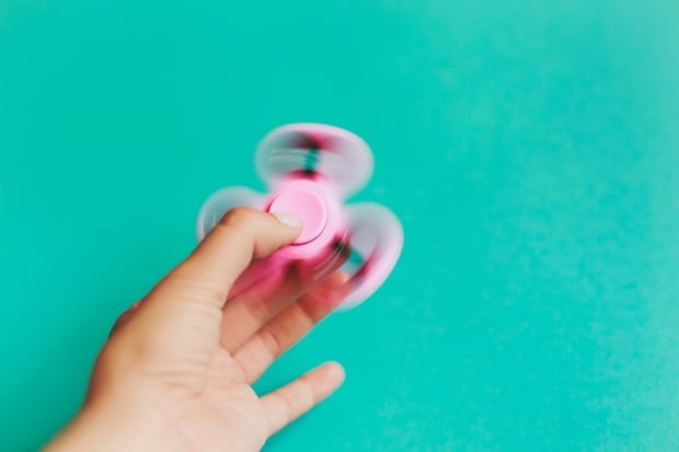 Fidget spinner, spinning in hand on trendy pastel blue background.