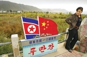A Chinese woman looks at the Chinese and North Korean National flags on the Chinese/North Korean border in the town of Tu Men in China's northeast Jilin province 12 October 2006.  A collapsing North Korea is a nightmare China hopes will never come true, as it could lead to military and political chaos on its doorstep, analysts said as North Korea's declared nuclear test this week highlighted an entire range of violent scenarios, one scarier than the other, and all with direct implications for China's national security. AFP PHOTO/Peter PARKS







