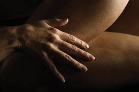 Close up of Caucasian female hand on nude Hispanic female thigh.