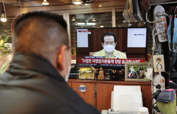 정부가 현행 사회적 거리두기 단계를 설 연휴가 끝날 때까지 2주 더 연장하겠다고 밝힌 지난달 31일 서울 광장시장에서 한 상인이 TV로 거리두기 연장 발표를 시청하고 있다. 사진=뉴스1