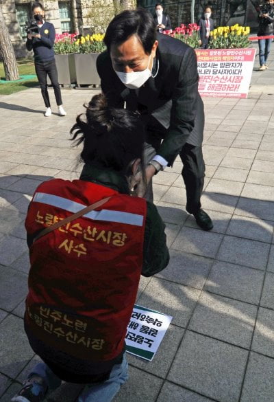 오세훈 서울시장이 8일 서울 중구 서울시청으로 출근하다 엎드려 절하는 노량진 수산시장 상인을 일으켜 세우고 있다. 연합뉴스