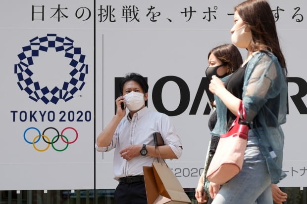 일본 수도 도쿄에서 마스크를 쓴 시민들이 도쿄올림픽의 포스터 앞을 지나고 있다. 사진=AP