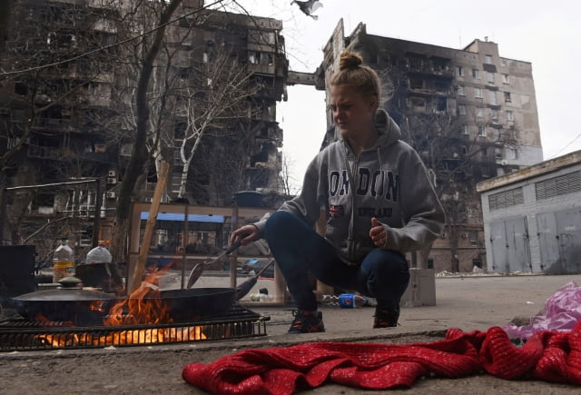 우크라이나 남부 항구도시 마리우폴의 한 주민이 3일(현지 시각) 실외에 지핀 불로 음식을 만들고 있다. / 사진=연합뉴스