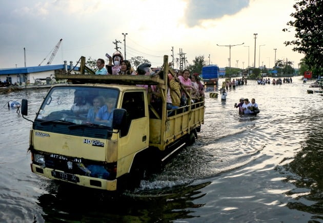 6월 20일 인도네시아 중부 자바 세마랑 해안의 탄중 에마스 항구에서 만조로 인한 홍수로 사람들이 차량을 타고 홍수를 헤치고 있다. 사진=연합뉴스 제공