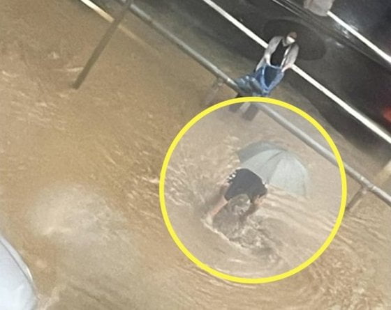 경기도 의정부시의 한 도로가 침수되자 한 중년 남성(노란 원)이 직접 배수로의 쓰레기를 치우고 있다. 그 뒤에는 다른 여성이 종량제 봉투를 들고 서 있다. / 사진=온라인 커뮤니티