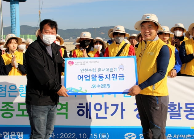 김진균 수협은행장(오른쪽)과 임직원들이 지난 15일 인천 중구 영종해안북로 삼목항 방조제 일대에서 환경정화활동을 펼친 뒤 인천수협 산하 운서어촌계에 어업활동지원금을 전달하고 있다. 수협은행 제공