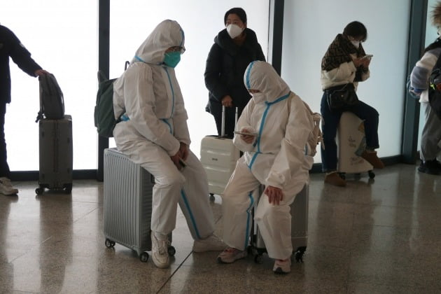 11일(현지시간) 중국 후베이성 우한의 한 기차역 대기실에 방역복을 입은 사람들이 여행용 트렁크에 앉아 기다리고 있다. /사진=연합뉴스