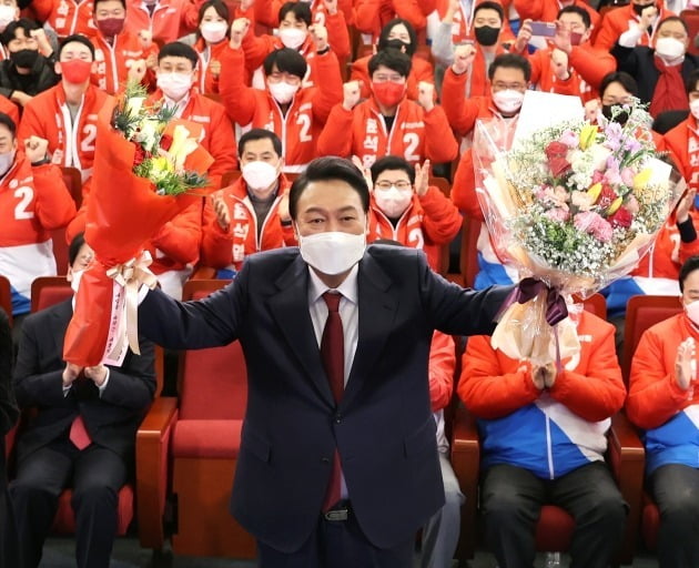 지난해 3월10일 윤석열 대통령이 서울 여의도 국회도서관에 마련된 '국민의힘 제20대 대통령선거 개표상황실'을 찾아 꽃다발을 받은 뒤 취재진을 향해 포즈를 취하고 있다. 연합뉴스