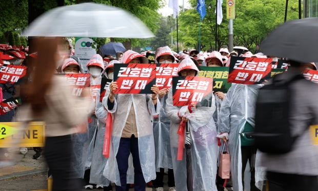  25일 오후 서울 여의도 국회 앞에서 열린 간호법저지 전국간호조무사 대표자 연가투쟁에서 시민들이 피켓을 든 참가자 앞을 지나고 있다. /사진=연합뉴스