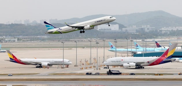 지난달 24일 오후 인천국제공항 주기장에 세워진 대한항공, 아시아나항공 여객기 위로 에어부산 여객기가 이륙하고 있다. 사진=연합뉴스