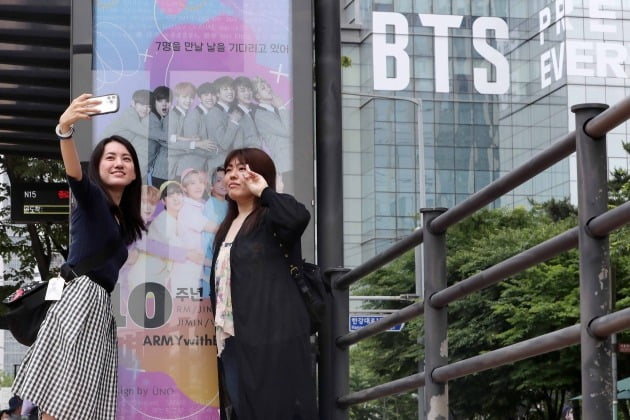 BTS 해외 팬들이 12일 서울 용산구 하이브 사옥에서 BTS 데뷔 10주년을 축하하는 광고판을 배경으로 사진을 찍고 있다./뉴스1