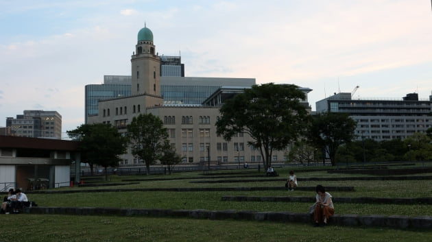 해지기 전 공원에서 독서를 즐기는 시민들 뒤로 세관 건물이 보인다. / JAPAN NOW