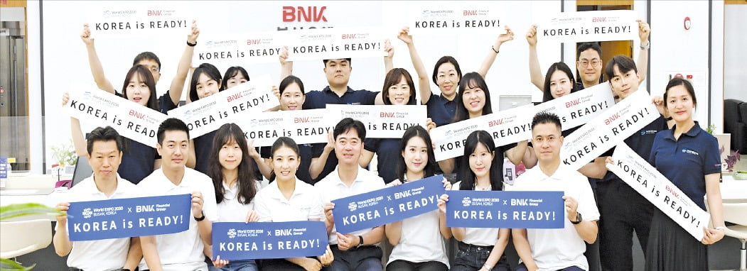 BNK금융그룹 임직원이 ‘2023부산세계박람회’ 유치 응원 티셔츠를 입고 기념촬영을 하고 있다. 임직원들은 박람회 유치에 대한 관심도를 높이기 위해 응원 티셔츠를 착용하고 각종 업무회의와 행사 등에 참석하고 있다. /BNK금융 제공 