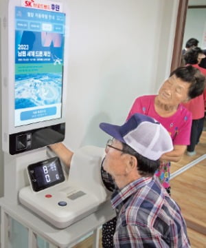 한 노인이 전북 남원시 경로당에 설치된 온애드를 보면서 혈압을 측정하고 있다.  SK브로드밴드 제공 