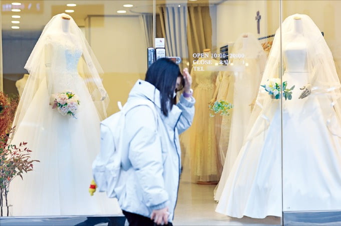 11일 서울 아현동 웨딩거리에 있는 웨딩드레스 판매점 앞을 한 시민이 지나가고 있다. 통계청이 이날 발표한 ‘2022년 신혼부부 통계’에 따르면 결혼한 지 5년 이하 신혼부부가 지난해 낳은 자녀 수는 평균 0.65명에 그친 것으로 나타났다.   연합뉴스 