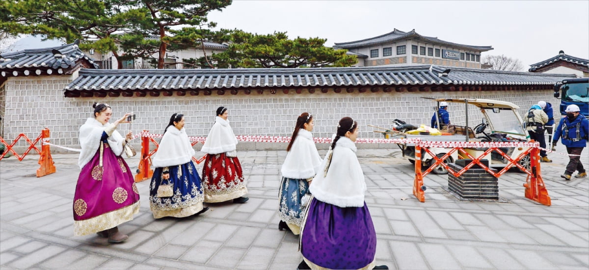 한복을 차려입은 외국인 관광객들이 4일 1차 복구 작업을 마치고 가림막 철거가 진행 중인 경복궁 담벼락 앞을 지나가고 있다. 지난해 말 ‘낙서 테러’로 훼손된 경복궁 담벼락은 20여 일간의 복구를 통해 80%가량 복원됐다. 문화재청은 1억원으로 예상되는 복구 비용을 낙서범들에게 물릴 방침이다.   뉴스1 