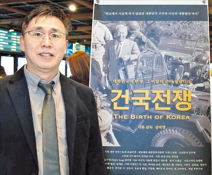 다큐멘터리 독립영화 ‘건국전쟁’ 포스터 앞에 서 있는 김덕영 감독.   다큐스토리 제공 