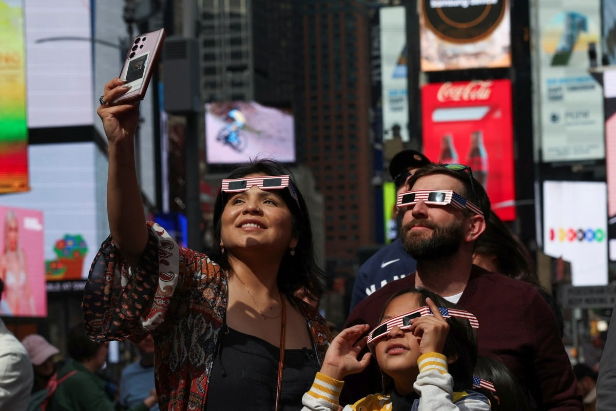 지난 8일 미국 뉴욕 타임스퀘어에서 달이 태양 일부를 가리는 부분일식을 보기 위해 한 여성이 스마트폰을 쓰고 있다. /로이터