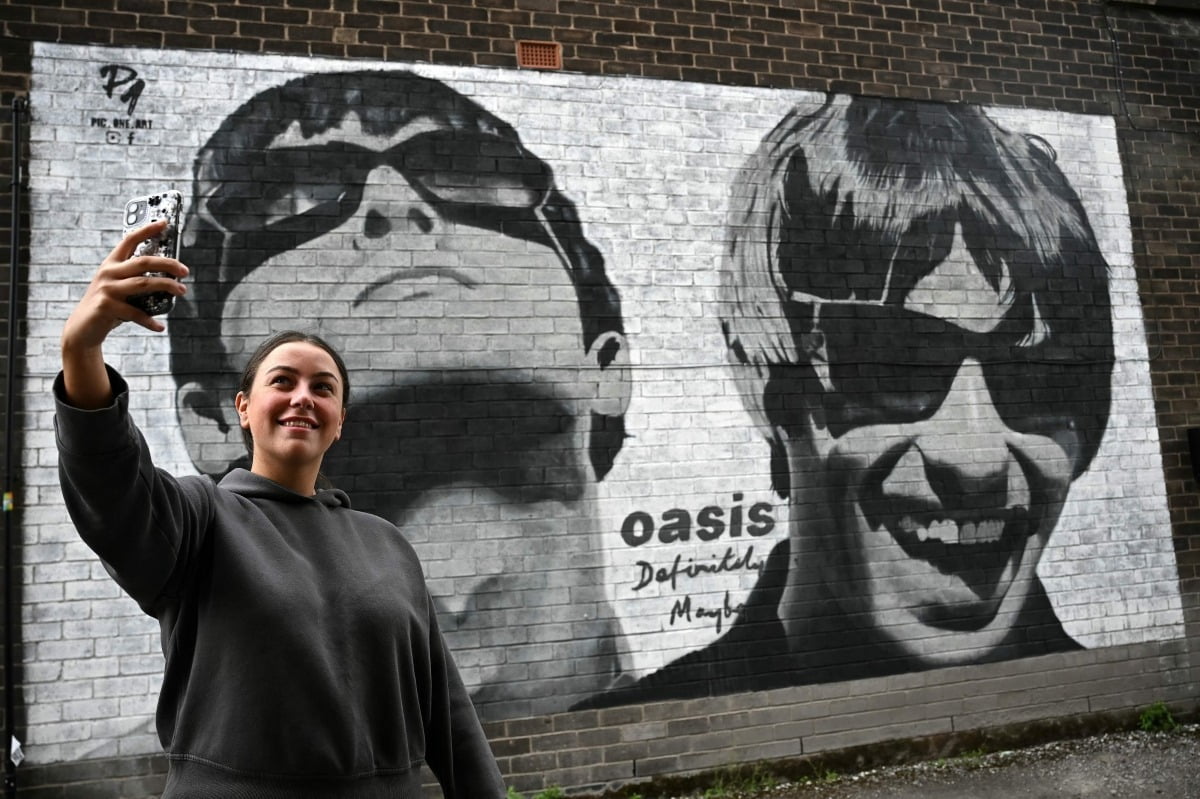 Um fã tira uma foto em frente ao mural dos irmãos Gallagher em Manchester. /Fotos=AFP