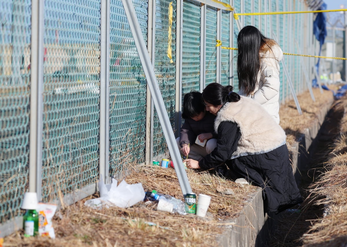 전남 무안국제공항 울타리 밖에서 한 가족이 희생자를 추모하고 있다. 사진=연합뉴스